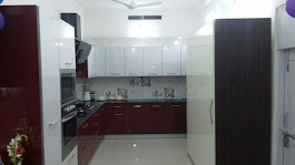 L-shaped modular kitchen with maroon and white cabinets, chimney, and built-in hob at Majestic Kitchens showroom